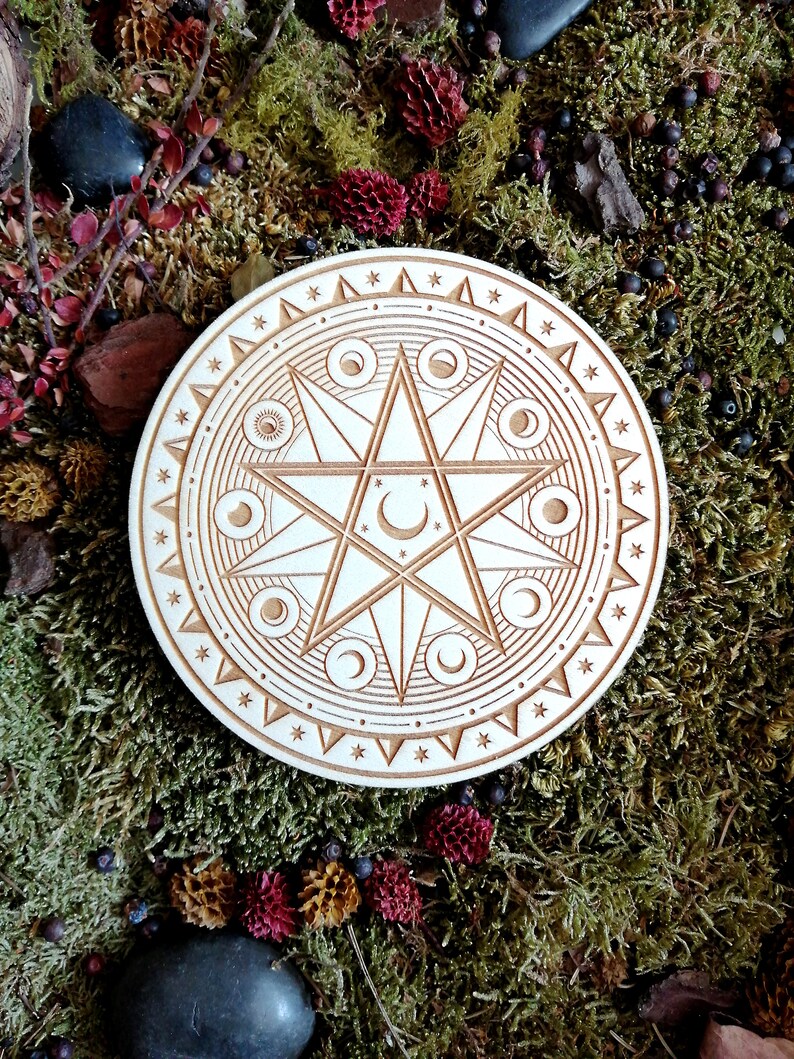 May include: A wooden circle with a carved design of a six-pointed star surrounded by a circle of crescent moons. The circle is on a bed of green moss with small red and brown berries.