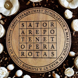 Puede incluir: Placa de madera redonda con el Cuadrado Sator, un cuadrado de palabras latinas con el pal&iacute;ndromo "SATOR AREPO TENET OPERA ROTAS." La placa est&aacute; rodeada de texto y adornos florales blancos.
