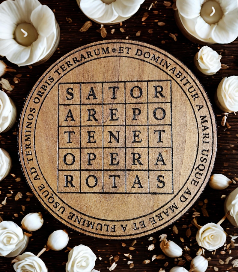 Puede incluir: Placa de madera redonda con el Cuadrado Sator, un cuadrado de palabras latinas con el pal&iacute;ndromo "SATOR AREPO TENET OPERA ROTAS." La placa est&aacute; rodeada de texto y adornos florales blancos.