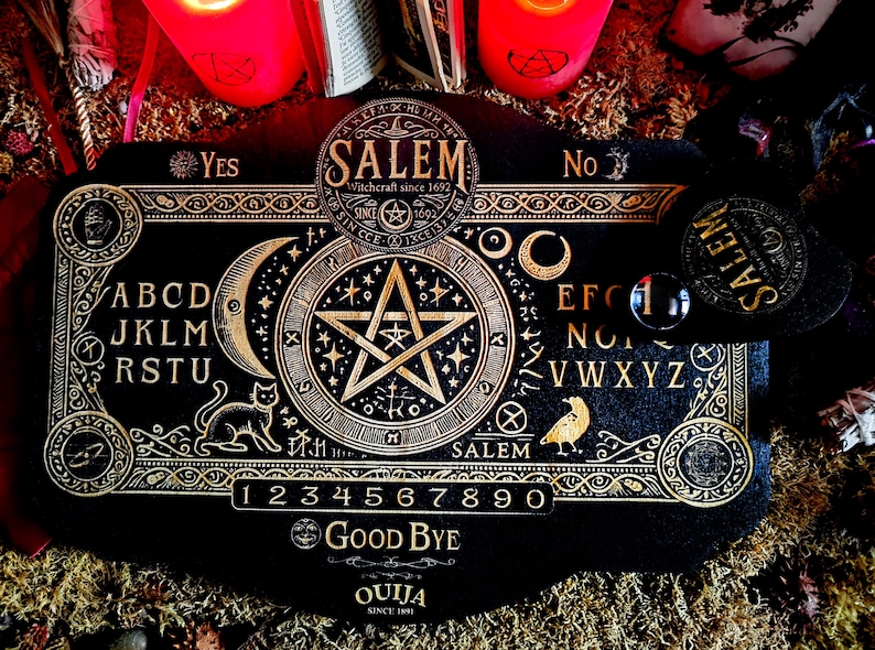 May include: A black wooden Ouija board with gold lettering and a pentagram design. The board features the alphabet, numbers 1-9 and 0, and the words "Yes", "No", "Good Bye", and "Ouija since 1901".