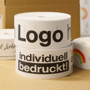 Könnte beinhalten: Weiße zylindrische Rollen mit schwarzem Text "Logo" und "individuell bedruckt!". Die Rollen sind gestapelt. Weitere Rollen mit Text und einem Regenbogen befinden sich im Hintergrund.