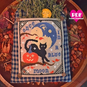May include: A cross-stitch pattern featuring a black cat, a pumpkin, and a blue moon with the text "Once in a Blue Moon".