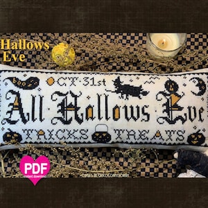 Puede incluir: Una almohada blanca con bordado negro que presenta el texto "All Hallows Eve" con un gato negro, una luna y calabazas. La almohada está sobre un fondo de tela a cuadros con flores secas.