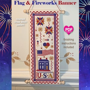 May include: A vertical counted cross stitch banner titled Flag & Fireworks Banner. The fabric features a red, white, and blue design with fireworks, a heart, an American flag, a house, and the text U.S.A. It hangs from wooden dowels.