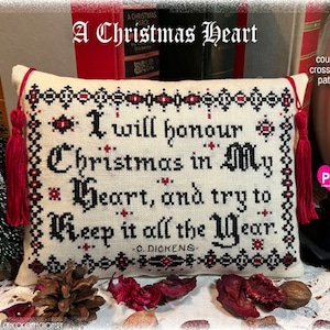 May include: A white pillow with red tassels features a cross stitch design with the quote "I will honour Christmas in my Heart, and try to Keep it all the Year." - C. Dickens. The pillow is a counted cross stitch pattern.