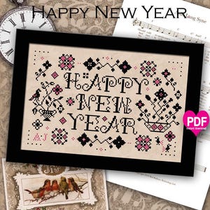 Könnte beinhalten: Ein Kreuzstichmuster für einen Sampler mit dem Text "Happy New Year" in schwarzen Buchstaben mit rosa und schwarzen floralen Akzenten. Das Muster ist auf beigefarbenem Hintergrund und beinhaltet einen PDF-Sofortdownload.