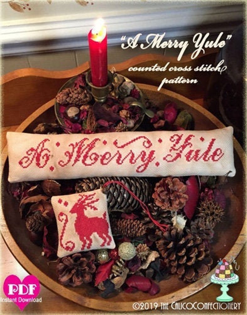 May include: A counted cross stitch pattern for a Christmas ornament with the text "A Merry Yule" in red lettering on a white background. The ornament is surrounded by pine cones and potpourri.
