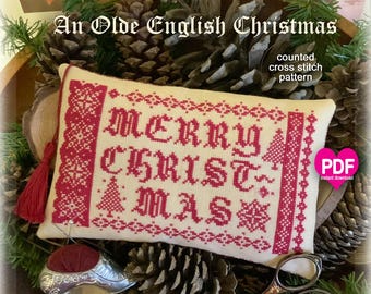 Pode incluir: Um padrão de ponto de cruz creme com as palavras "MERRY CHRISTMAS" em vermelho. O design inclui árvores de Natal e flocos de neve. O texto "An Olde English Christmas" está no topo. Um borla vermelha e uma dedaleira de prata são visíveis.
