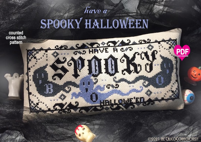 May include: A rectangular counted cross stitch pattern on cream fabric featuring the text "HAVE A SPOOKY HALLOWEEN" in black and blue gothic lettering, surrounded by black and blue ghost illustrations and a decorative border, with a pink PDF icon.