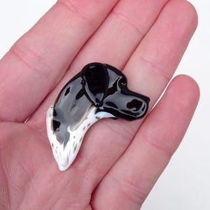 Könnte beinhalten: Glänzende, schwarz-weiße Hunde-Kopf-Figur. Der Kopf des Hundes ist schwarz mit weißen und braunen gefleckten Markierungen am unteren Teil. Die Figur wird in einer Hand gehalten.