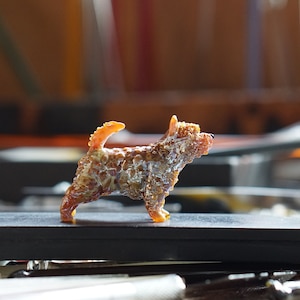 以下が含まれることがあります： 茶色と白のモザイク模様の小さな犬の置物。置物は、不規則な形をした小さなガラスやセラミックの破片で作られています。