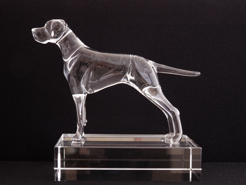 May include: A clear glass sculpture of a dog standing on a clear glass base. The dog is in a running pose with its head turned to the side.