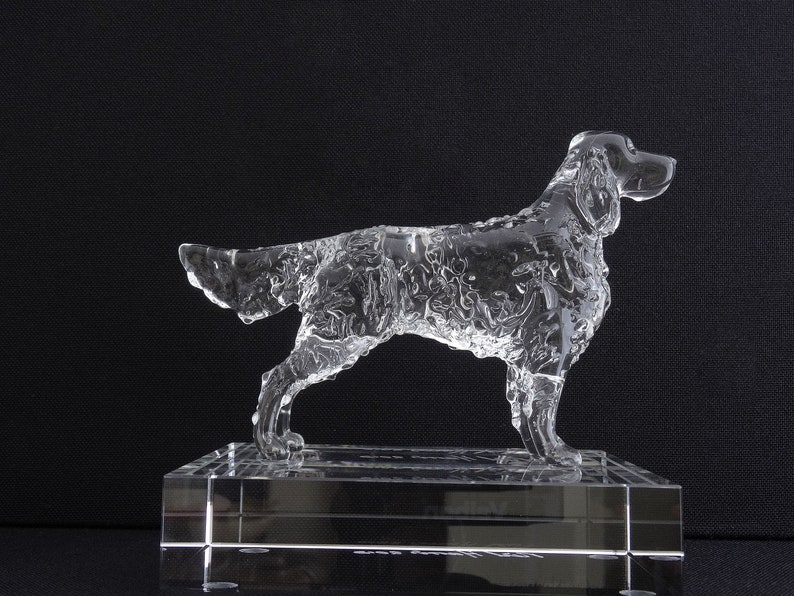 Puede incluir: Una escultura de perro de cristal transparente de pie sobre una base de cristal transparente. El perro est&aacute; en una pose de carrera con la cabeza girada hacia un lado.