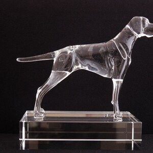 May include: A clear glass sculpture of a dog standing on a clear glass base. The dog is in a running pose with its head turned to the side.
