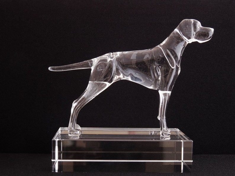 May include: A clear glass sculpture of a dog standing on a clear glass base. The dog is in a running pose with its head turned to the side.