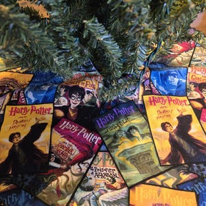May include: A circular Christmas tree skirt featuring various book covers from the Harry Potter series. The skirt has a black lace trim and is decorated with images from the books, including "Harry Potter and the Sorcerer's Stone" and "Harry Potter and the Deathly Hallows."