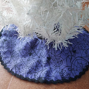 May include: Purple and black Christmas tree skirt with a spiderweb design. The skirt has a black lace trim.