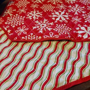 May include: Red and white quilted table runner with a snowflake pattern on one side and red and green stripes on the other side.