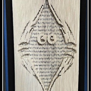 Op de afbeelding: Een ingelijst kunstwerk met een boek dat is gevouwen tot een ruitvorm met een centraal ontwerp. De pagina's zijn gesneden en gevouwen om de afbeelding te creëren, met zichtbare tekst. Het kunstwerk zit in een zwart frame met een blauwe rand.