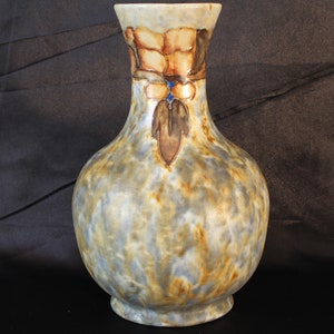 May include: A ceramic vase with a bulbous body and a narrow neck. The vase is decorated with a mottled glaze in shades of blue, brown, and white. The neck of the vase features a floral design in shades of orange, brown, and blue.