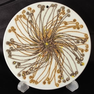 Può includere: Un piatto in ceramica bianca con un design a spirale di linee marroni e gialle. Le linee creano uno schema radiale, che ricorda un fiore o una stella.