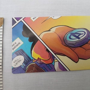 May include: A comic book panel featuring a hand holding a blue and silver disc with the letter "A" in the center. The text "Well... listen..." is in a speech bubble.