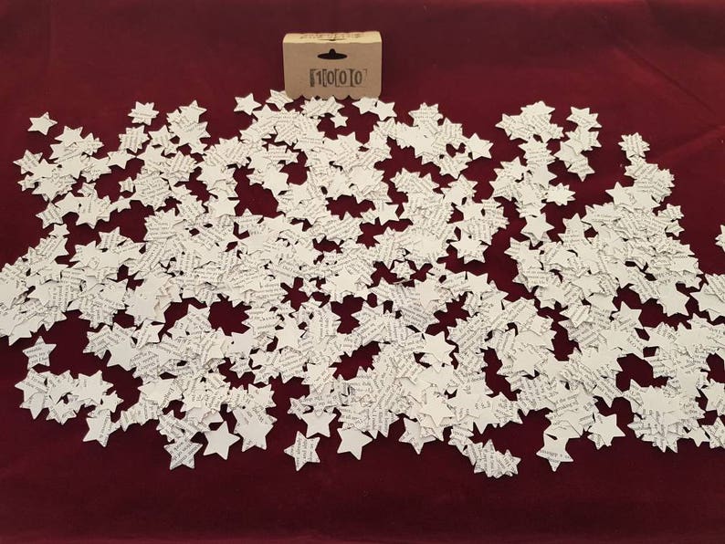 May include: A large quantity of white paper stars scattered on a red surface. The stars are made of paper and have a printed design. A small brown box with the word "MOOLO" printed on it is in the upper center of the image.