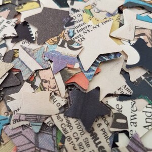 May include: A pile of confetti made from recycled paper, printed with text and images. The confetti is in the shape of stars and is mostly white with black, red, and blue accents.