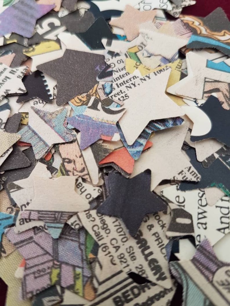 May include: A pile of confetti made from recycled paper, printed with text and images. The confetti is in the shape of stars and is mostly white with black, red, and blue accents.