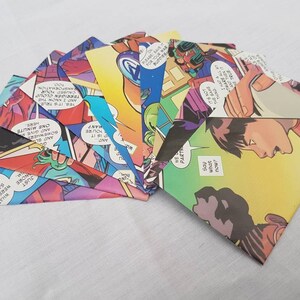 May include: A collection of eight colorful envelopes made from comic book pages. The envelopes are folded and arranged in a fan shape. The comic book pages feature colorful illustrations and text.
