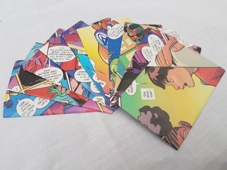 May include: A collection of eight colorful envelopes made from comic book pages. The envelopes are folded and arranged in a fan shape. The comic book pages feature colorful illustrations and text.