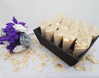 May include: A black tray filled with paper cones filled with white flower petals. The cones are made from recycled book pages. A bouquet of purple and white felt flowers is in the foreground.