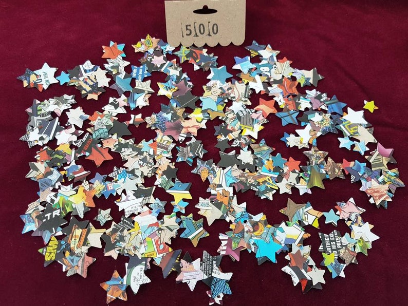 May include: A large quantity of confetti stars made from recycled comic book pages. The stars are scattered on a red surface.
