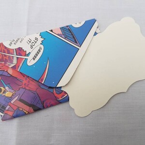 May include: A handmade envelope made from a comic book featuring a colorful illustration of a robot with the text "GRRRR... STOP it!"  The envelope is open and a blank white card with a scalloped edge is inside.