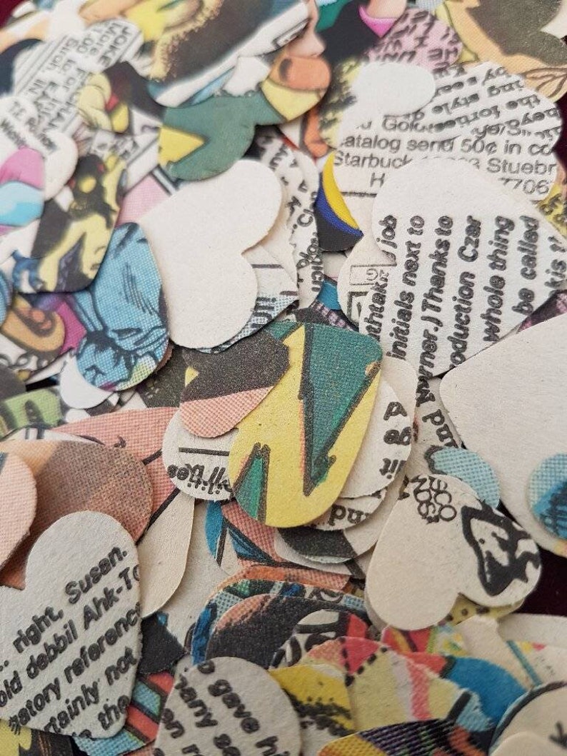 May include: A pile of heart-shaped confetti made from recycled comic book pages. The confetti is in various colors, including red, blue, green, yellow, and black. The confetti is printed with text and images from comic books.