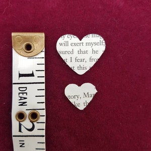 May include: Two paper hearts cut from a book page. The larger heart is 2 inches tall and the smaller heart is 1 inch tall. The hearts are on a red background.