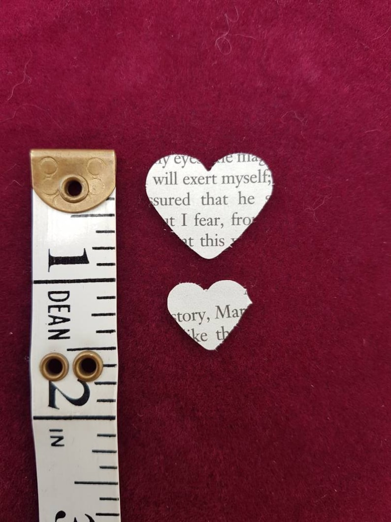 May include: Two paper hearts cut from a book page. The larger heart is 2 inches tall and the smaller heart is 1 inch tall. The hearts are on a red background.