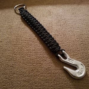 May include: A black paracord keychain with a silver hook. The hook has the text "618 P" engraved on it.