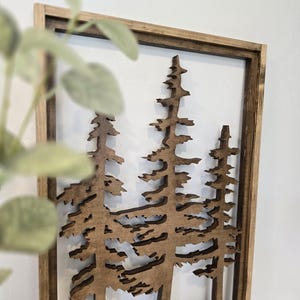 May include: A wooden wall decor featuring a cutout design of three pine trees in a brown frame.