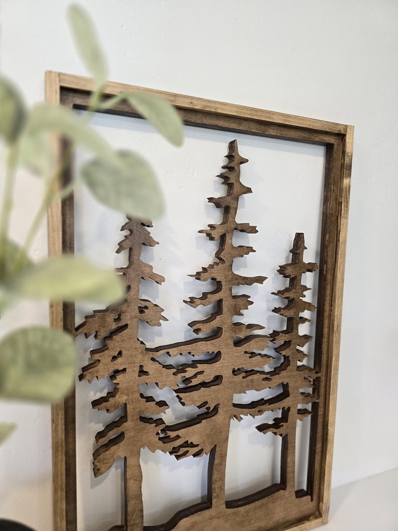 May include: A wooden wall decor featuring a cutout design of three pine trees in a brown frame.