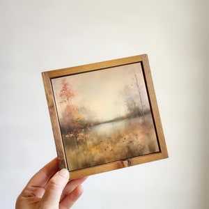 May include: A framed painting of a landscape with a lake and trees in muted tones of brown, orange, and gray.