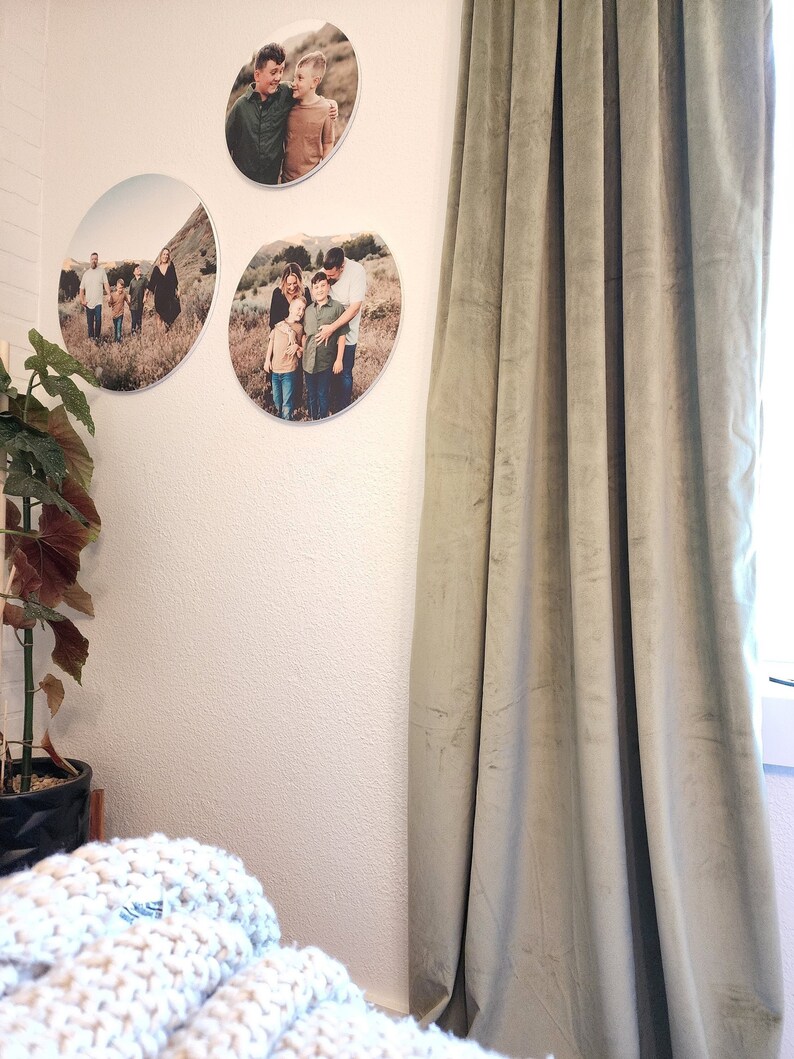May include: Three round canvas prints with photos of a family in a field. The prints are hanging on a white wall with a green velvet curtain to the right.