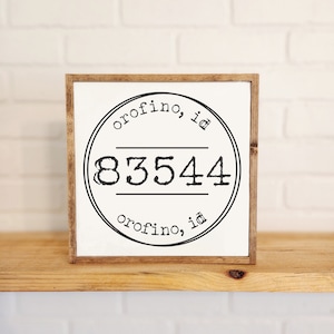 May include: A white sign with a brown wooden frame. The sign has a black circle with the text "Orofino, ID" and the number "83544" inside.