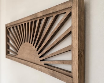 May include: A rectangular wooden wall art piece featuring a dark brown finish and a cutout design of a rising sun. The sun motif consists of a semi-circular base with radiating beams extending outward to the edges of the frame, creating a geometric pattern.