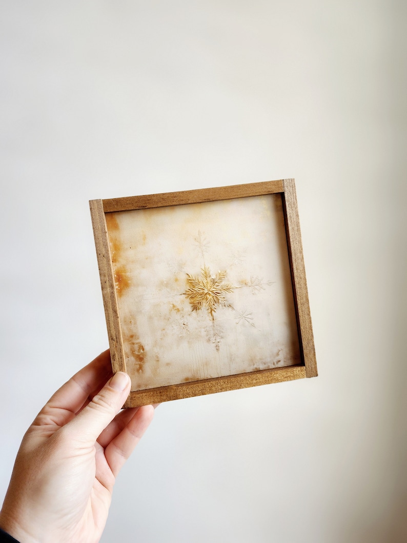 May include: A framed artwork featuring a gold snowflake on a white background.