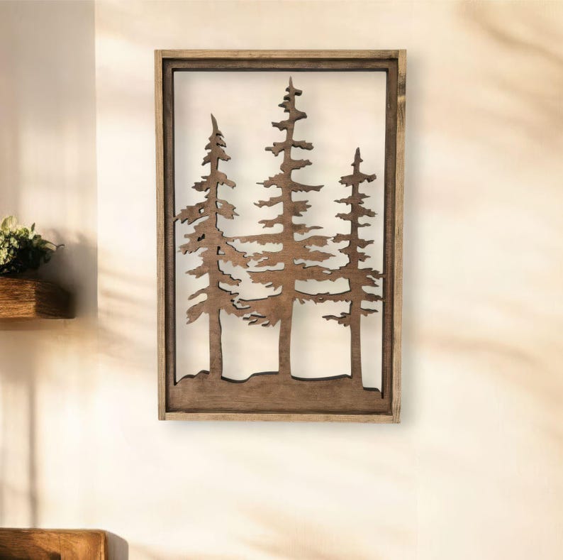 May include: A wooden wall decor featuring a cutout design of three pine trees. The trees are brown and the background is white. The decor is framed in a brown wood frame.