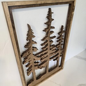 May include: A wooden wall decor featuring a silhouette of three pine trees with a brown wood frame.