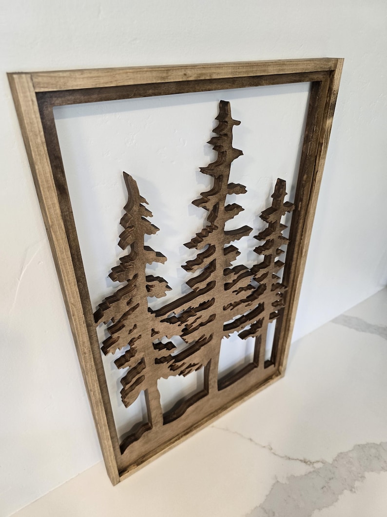 May include: A wooden wall decor featuring a silhouette of three pine trees with a brown wood frame.
