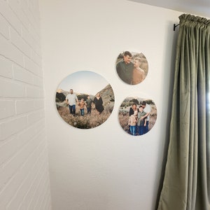 May include: Three round canvas prints with photos of a family in a field. The prints are hung on a white wall with a green curtain in the background.