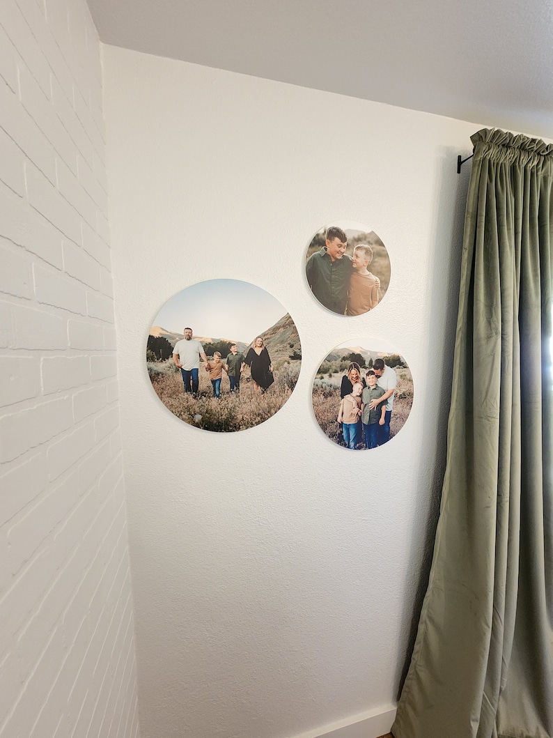 May include: Three round canvas prints with photos of a family in a field. The prints are hung on a white wall with a green curtain in the background.